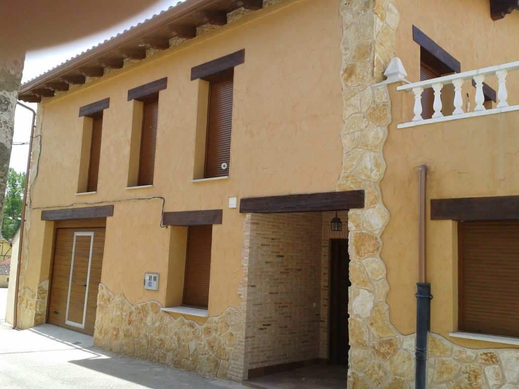 Fachada de casa con revoco ocre pintado y piedra – J.C. Sandín, pintura y pladur